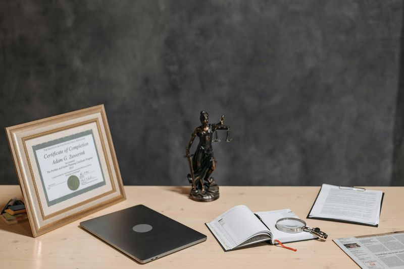 Mesa de advogado com estátua da Justiça, diploma, laptop e lupa sobre documentos jurídicos, ilustrando contexto de esclarecimento de mitos sobre isenção do IR.