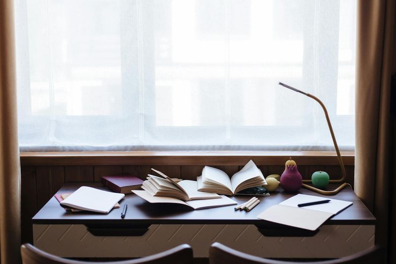 Mesa de estudo com livros e cadernos abertos sob luz natural da janela, ilustrando contexto de doença de Alzheimer relacionada à isenção do IR pela Lei 7.713/88.