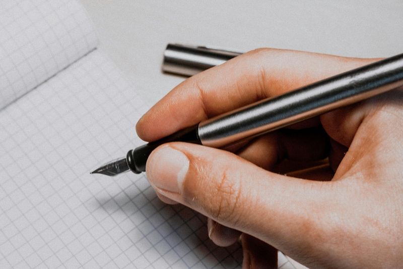 Mão escrevendo com caneta tinteiro sobre papel, ilustrando contexto de doença de Parkinson relacionada à isenção do IR pela Lei 7.713/88.